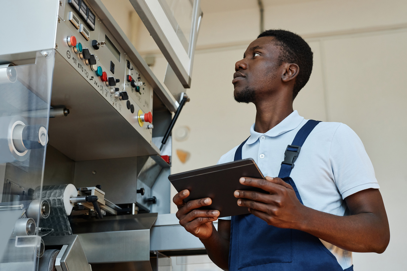 African American Factory Worker Holding Tablet Operating Machine Units